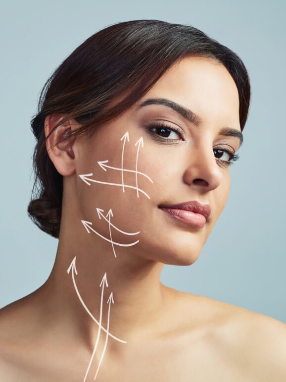 portrait-woman-skincare-with-arrow-plastic-surgery-studio-facial-treatment-beauty-filler-change-girl-lines-procedure-face-lift-medical-transformation-gray-background Portrait, woman and skincare with arrow for plastic surgery in studio, facial treatment and beauty filler of change. Girl, lines and procedure of face lift, medical transformation and gray background.