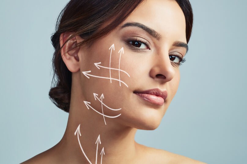 Portrait, woman and skincare with arrow for plastic surgery in studio, facial treatment and beauty filler of change. Girl, lines and procedure of face lift, medical transformation and gray background.