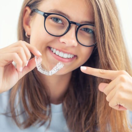 Dental invisible braces or silicone trainer in the hands of a young smiling girl. Orthodontic concept - Invisalign.